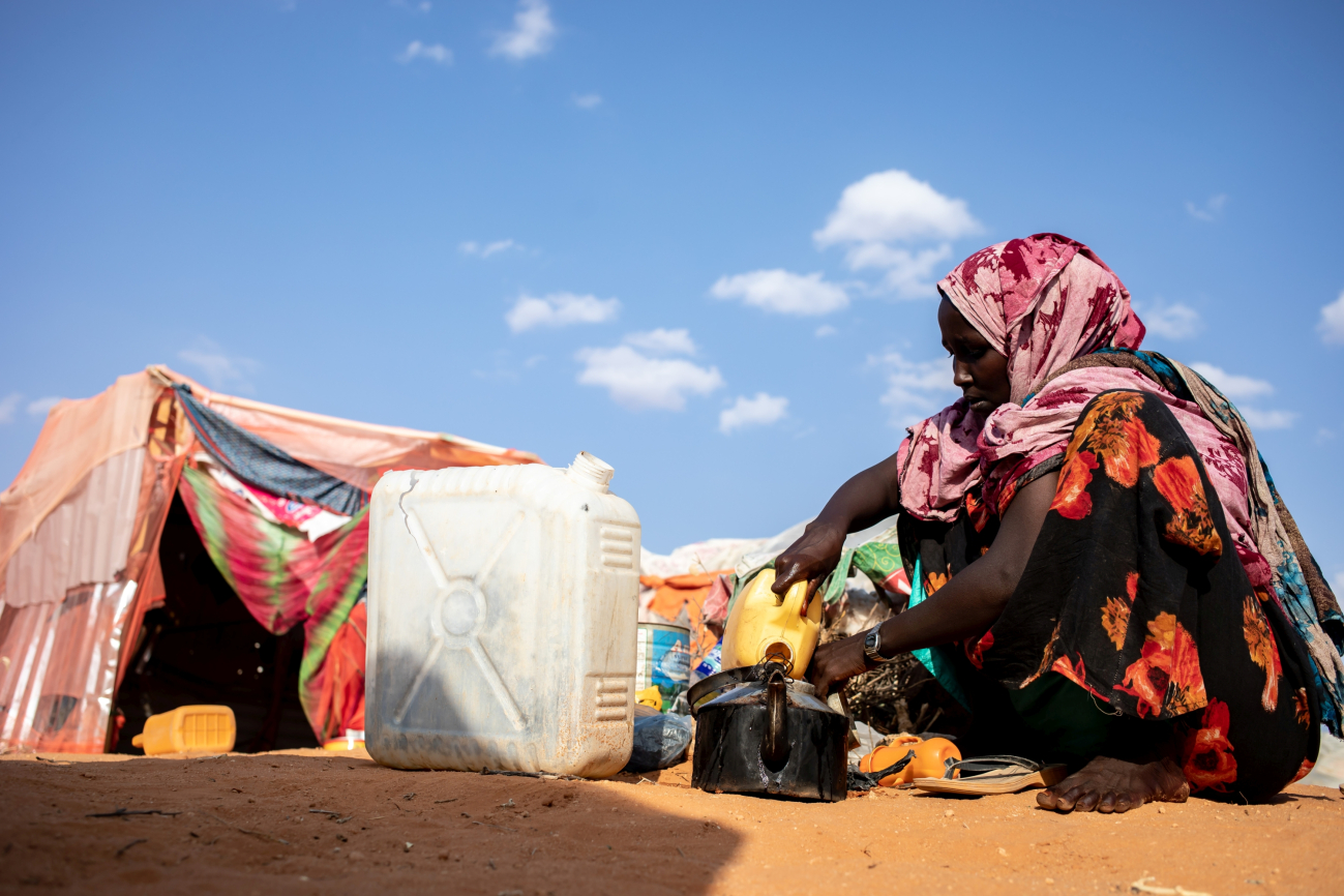 Somalische Frau sitzt mit Wasserkanistern vor ihrer provisorischen Unterkunft in einem Flüchtlingslager in Somalia.