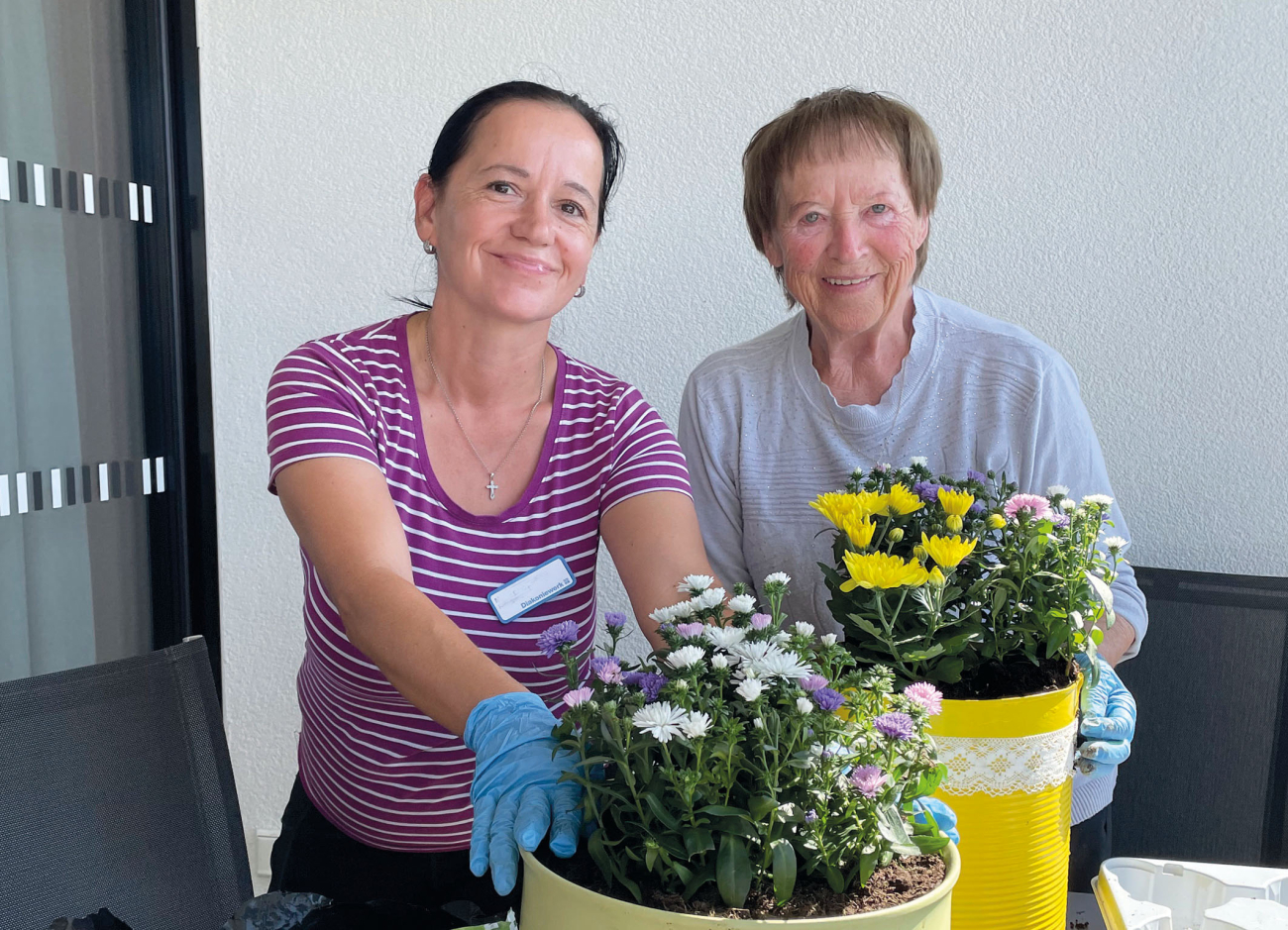 Eine Mitarbeiterin und eine Seniorin kümmern sich um Blumen
