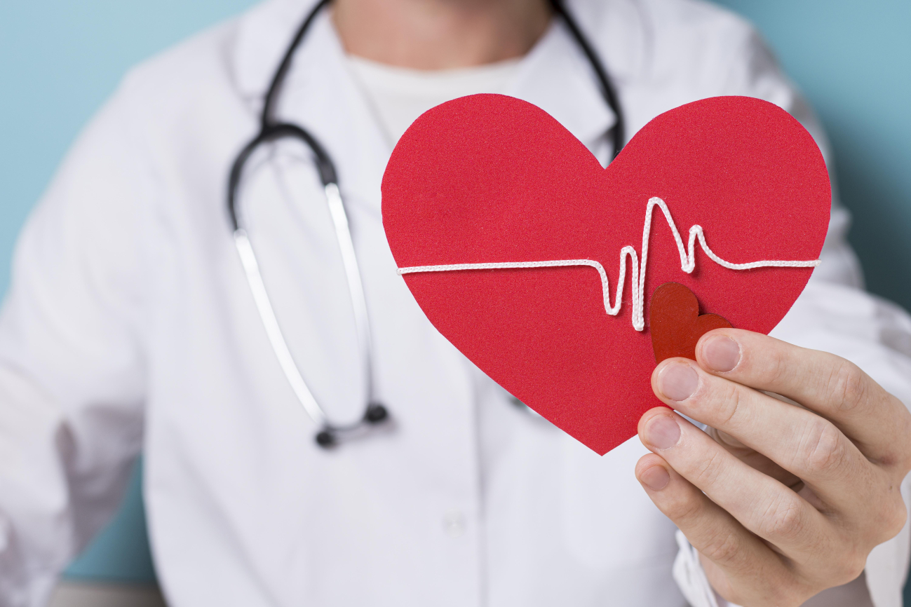 Arzt hält rotes Pappherz mit EKG-Lini in die Kamera