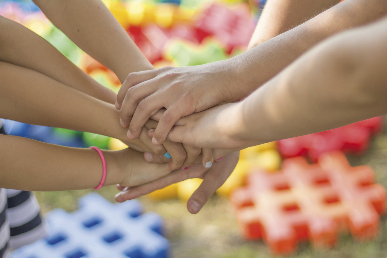 Kinderhände, die aufeinander liegen und zusammen halten mit buntem Hintergrund