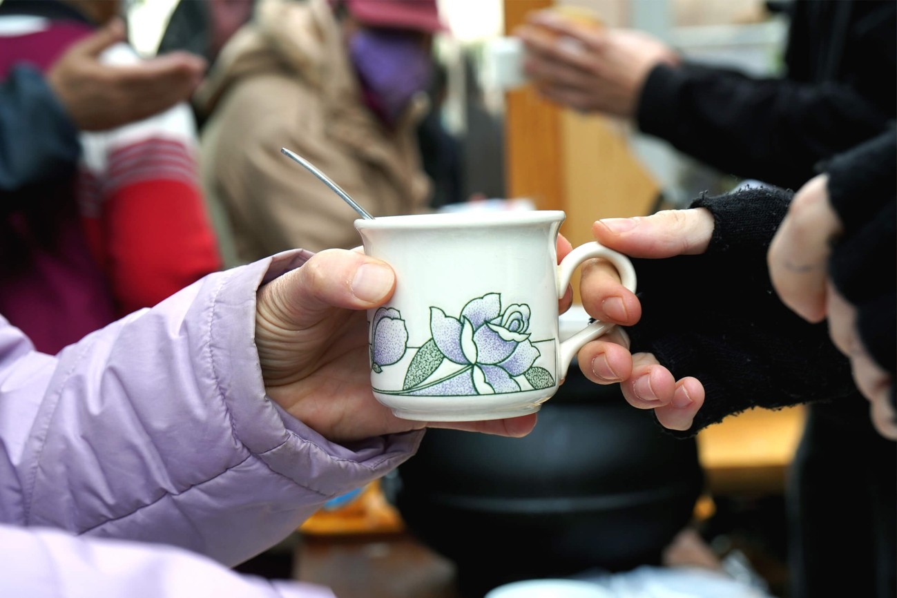 Eine Hand reicht einer anderen Hand eine Tasse mit einem warmen Getränk