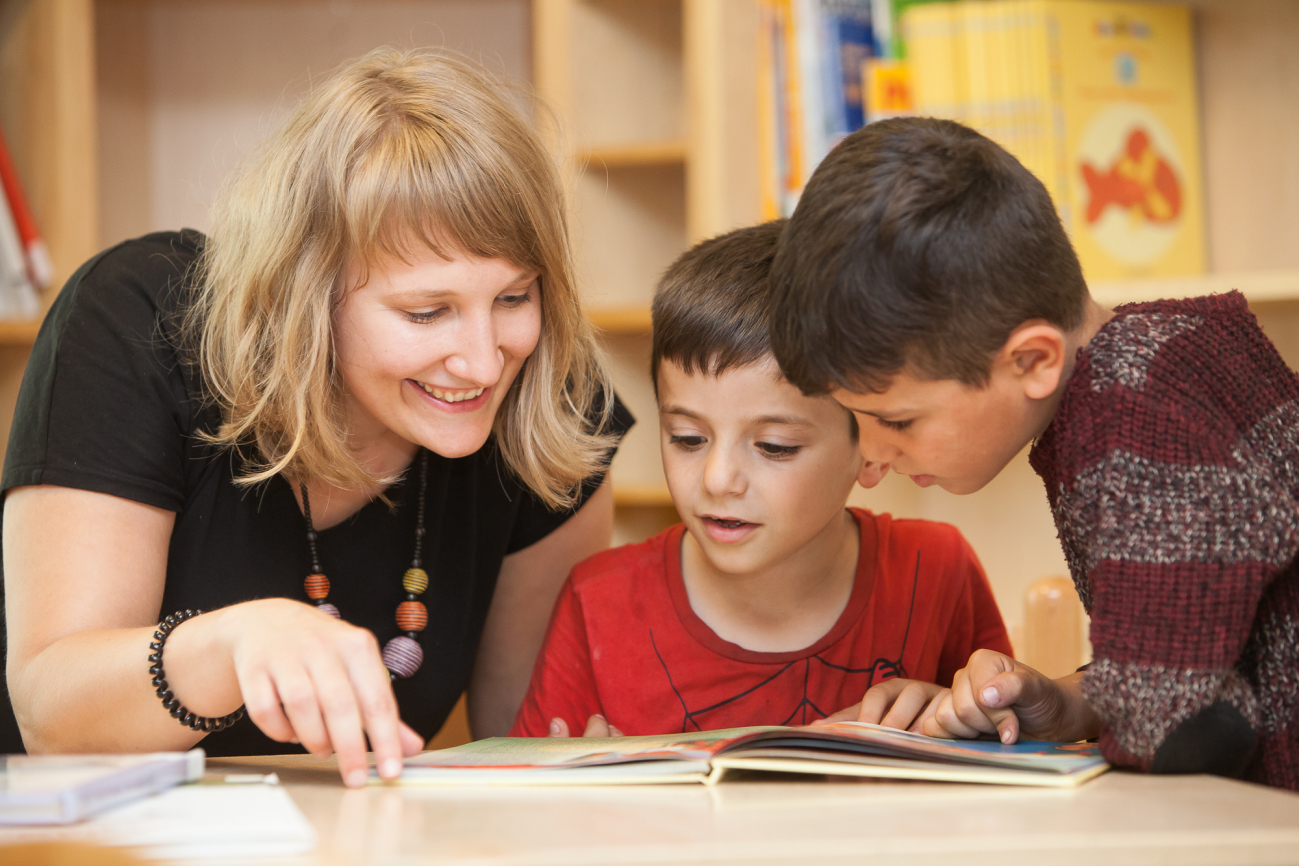 Frau schaut mit zwei Buben in ein Buch