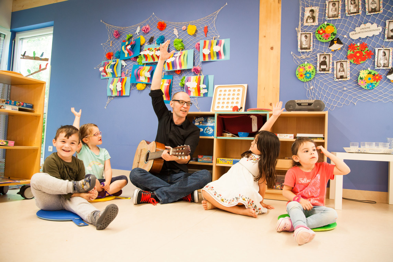 Kindergartenpädagoge spielt Gitarre und singt mit Kindern
