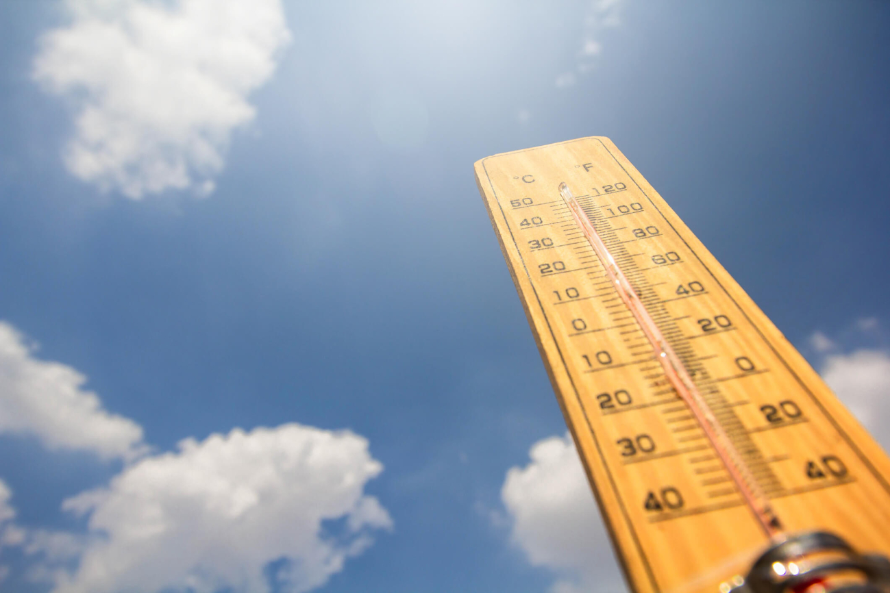 Die Sonne scheint, der Himmel ist blau und ein paar weiße Wolken ziehen vorbei. Daneben steht ein Thermometer, das in den Himmel zeigt.