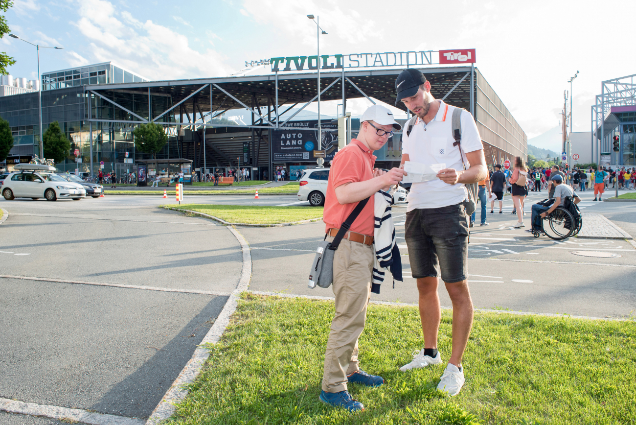 Diakoniemobil Mitarbeiter und Mann mit Behinderung warten auf den Einlass ins Fussballstadion.