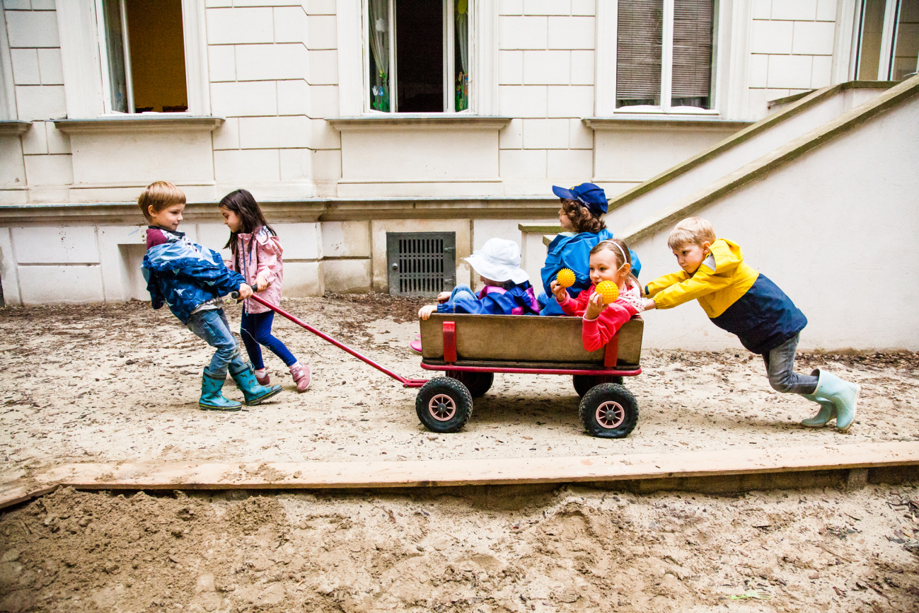 Eine Kindergruppe spielt mit Leiterwagen im Freien.
