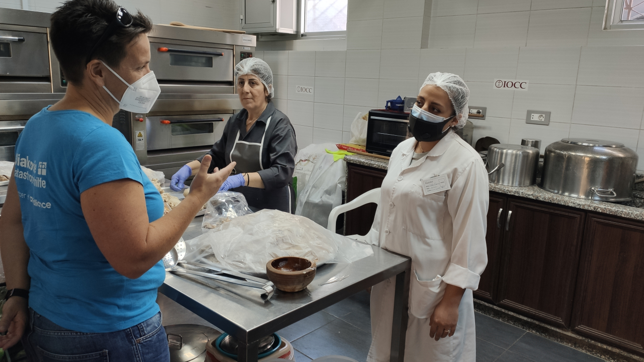Leiterin der Diakonie Katastrophenhilfe, Nina Hechenberger, im Gespräch mit zwei Frauen, die in der Gemeinschaftsküche Teig zubereiten