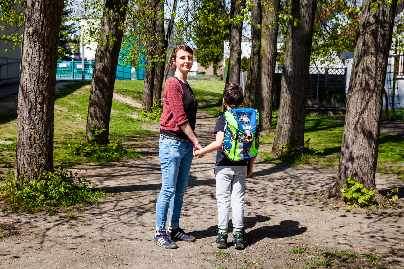 Frau begleitet Kind mit Schultasche auf dem Schulweg in einer Allee