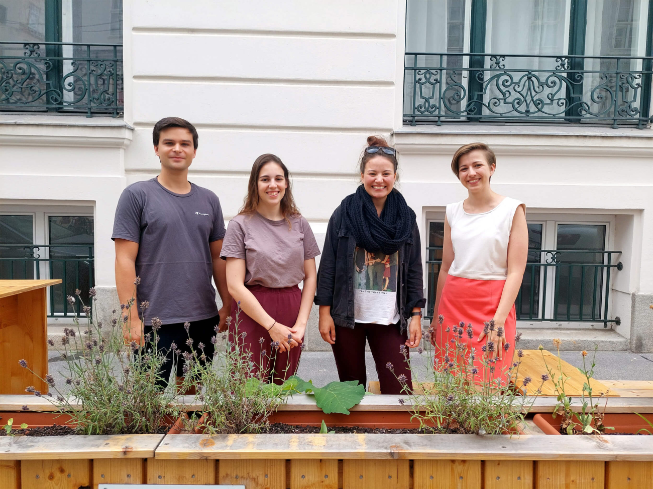 Vier junge Menschen stehen hinter Blumenkisten in der Stadt.