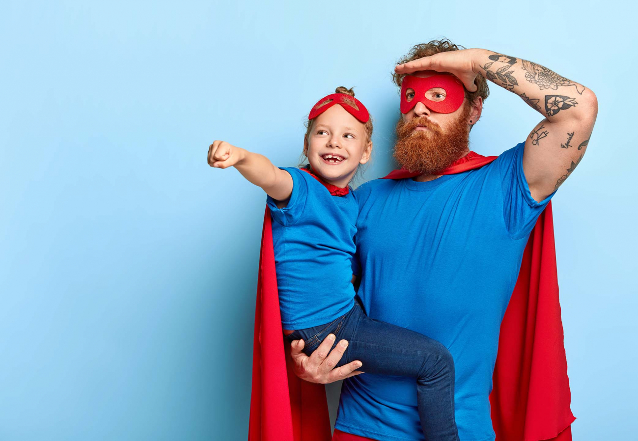Vater und Tochter beim Spiel mit Superheld:innen-Kostümen.