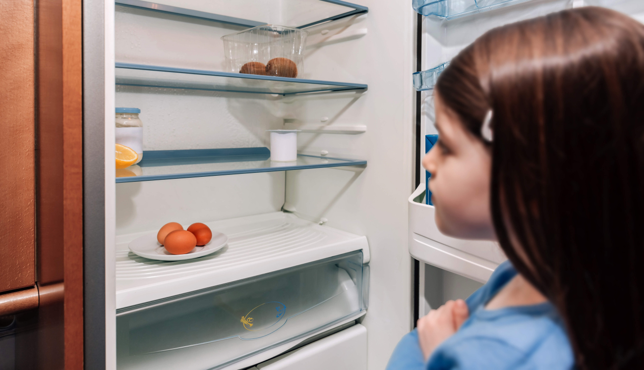 Ein Mädchens steht vor einem fast leeren Kühlschrank