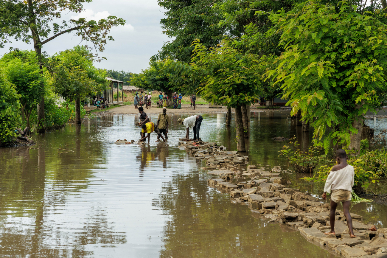 Männer errichten mit Händen einen Weg aus Steinen über eine überschwemmte Fläche.