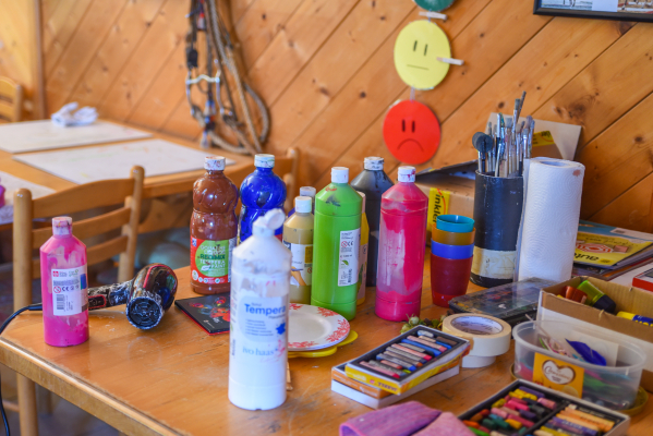Farben, Pinsel und Bastelmaterialien auf einem Holztisch in einem Raum mit Holzwänden