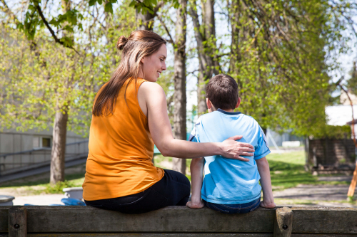 Eine Mitarbeiterin der Diakonie und ein Kind sitzen auf einer Bank im Garten.