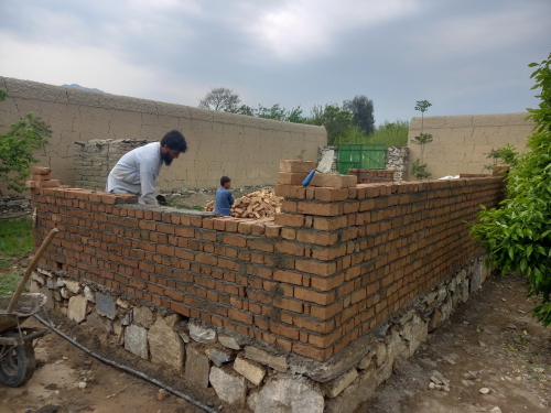 Ein Mann errichtet eine Ziegelmauer auf einem Fundament aus großen Steinen.