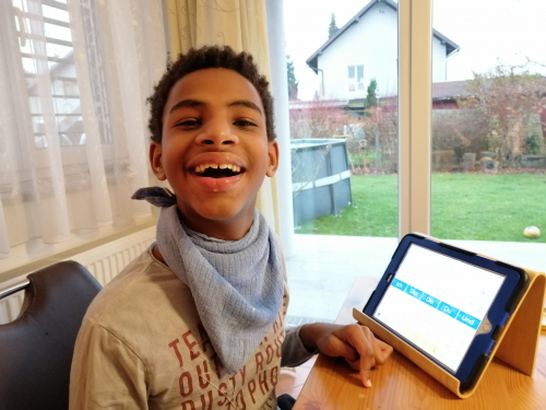 Jonathan sitzt vor seinem Ipad und lacht,