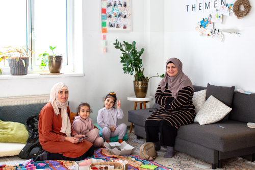 Zwei Frauen sitzen mit ihren Kindern auf dem Teppichboden im Frauencafe der Diakonie Frauenberatung