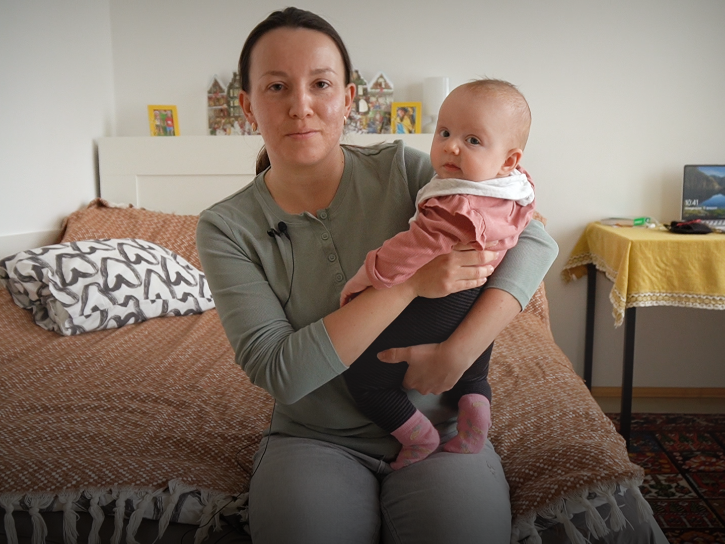 Frau sitzt mit Kleinkind am Arm auf einem Bett