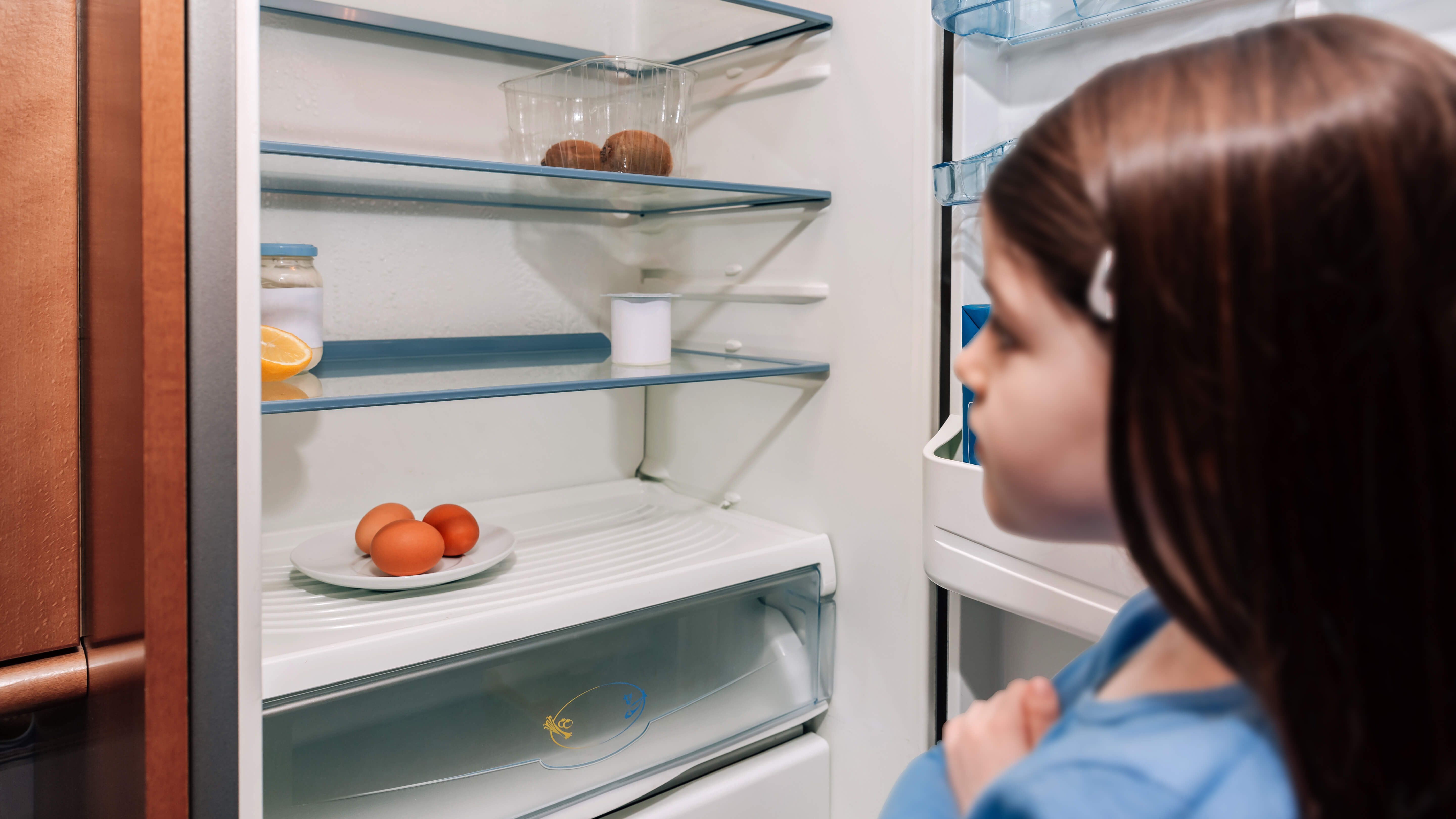 Ein Mädchens steht vor einem fast leeren Kühlschrank