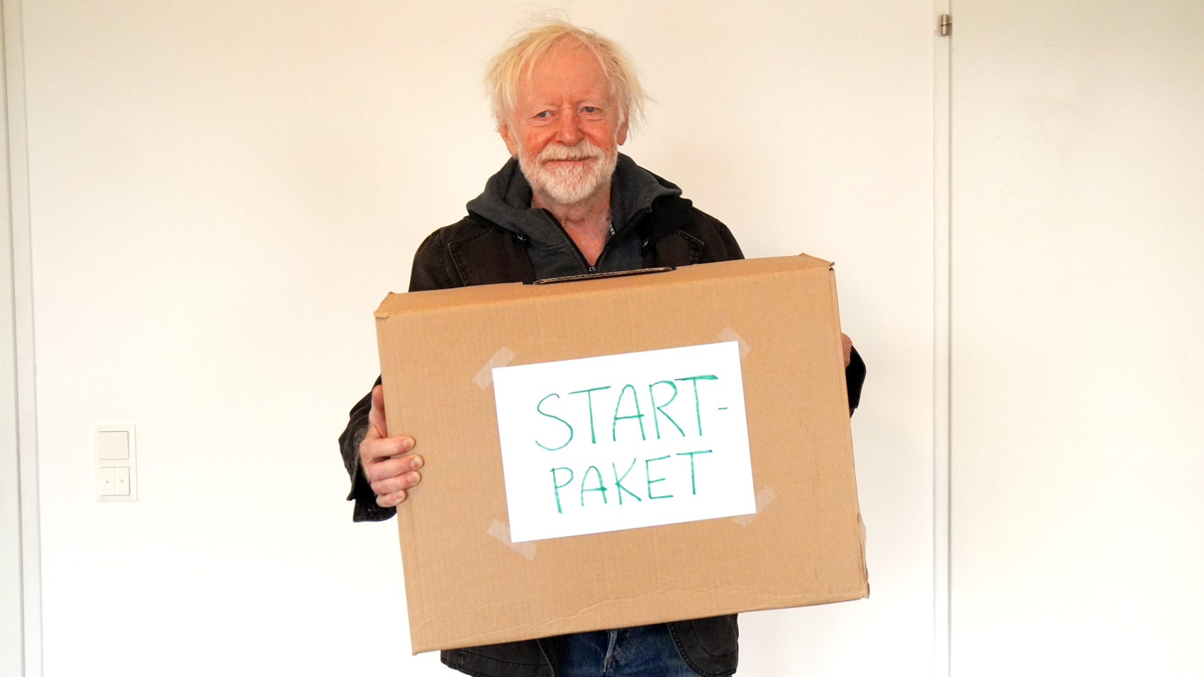 Ein Mann mit einem Umzugskarton wo "Startpaket" draufsteht