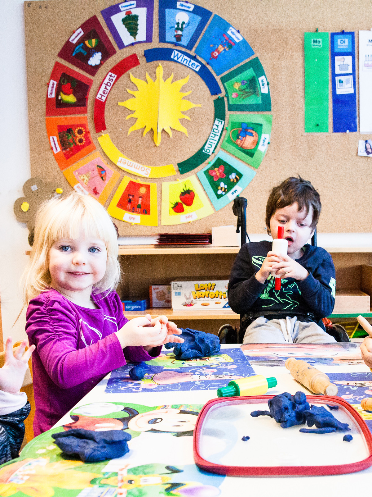 Kinder mit und ohne Behinderungen spielen mit Knetmasse gemeinsam an einem Tisch.