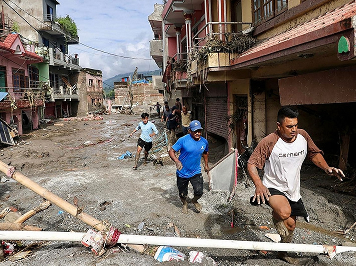 Einheimische gehen am 27. August 2026 in Devighat in der Stadt Bidur im nepalesischen Distrikt Nuwakot an Häusern vorbei, die nach Sturzfluten von Schlamm überschwemmt sind. Nach Angaben der nepalesischen Katastrophenschutzbehörde galten am 27. August noch 823 Menschen als vermisst, mehr als 24 Stunden nachdem eine tödliche Flut die Grenzregion zu Tibet heimgesucht hatte.