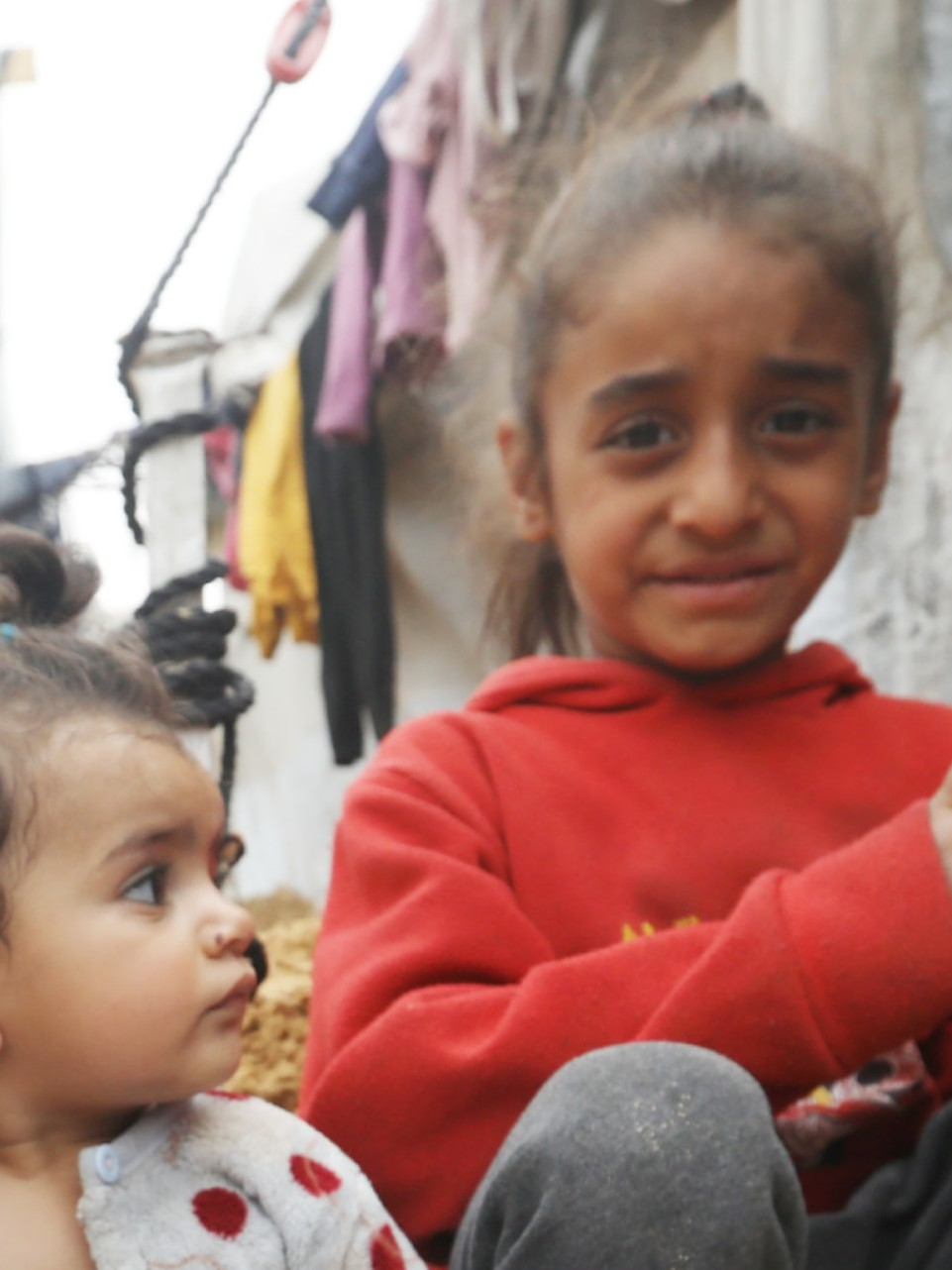 Kinder sitzen in Zeltlager auf dem Sandboden.
