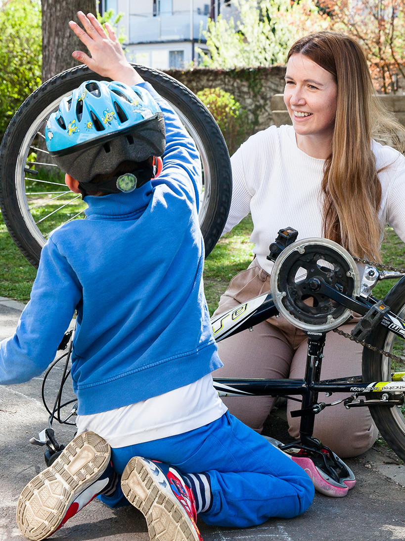 Junge mit Pädagogin bei Fahrrad am Boden kniend, probiert ob alles funktioniert.