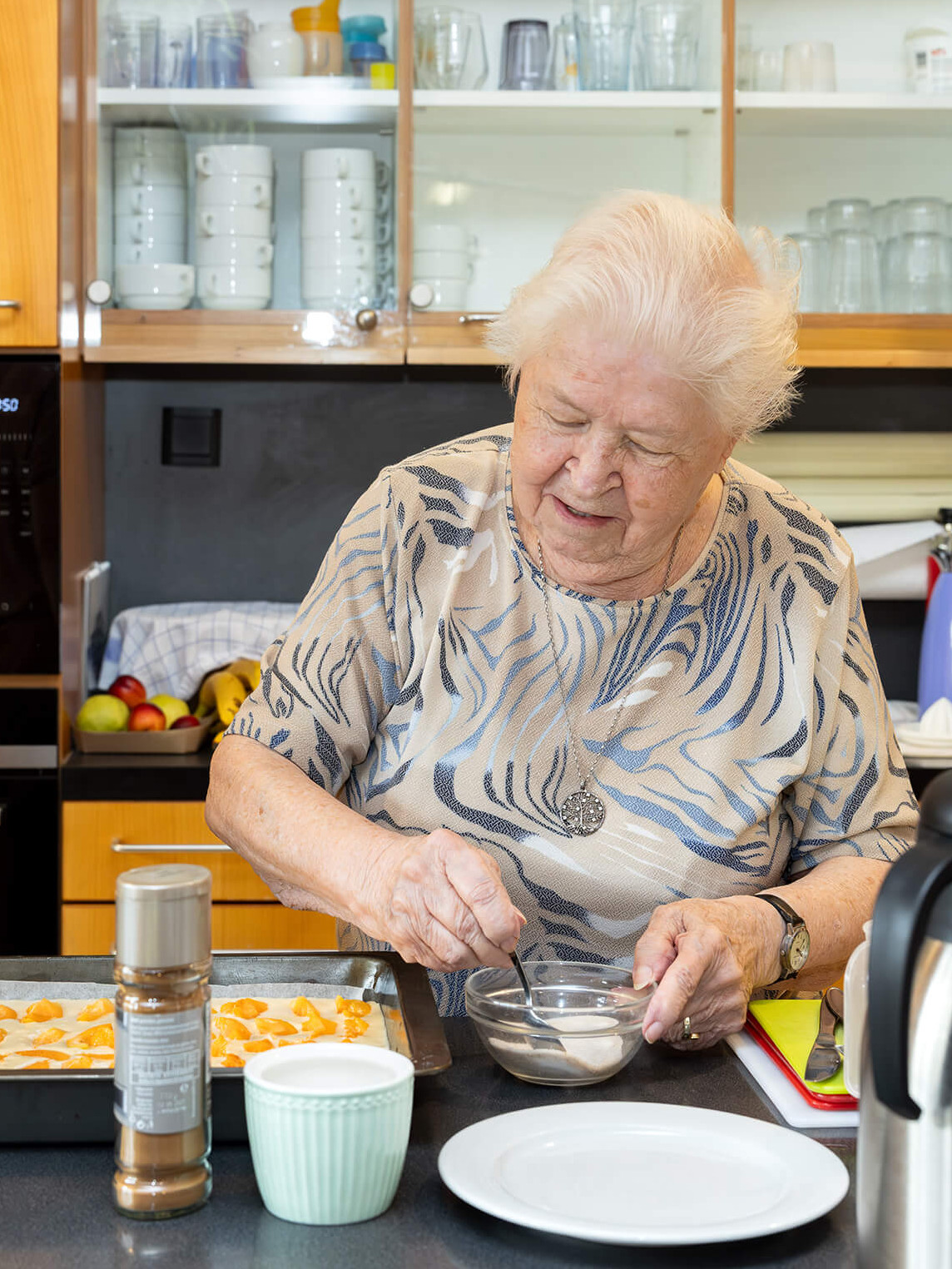 Eine ältere Dame backt einen Blechkuchen, und eine jüngere Dame steht daneben und spricht mit ihr.