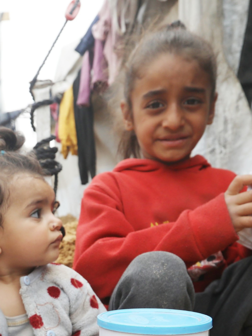 Kinder sitzen in Zeltlager auf dem Sandboden.