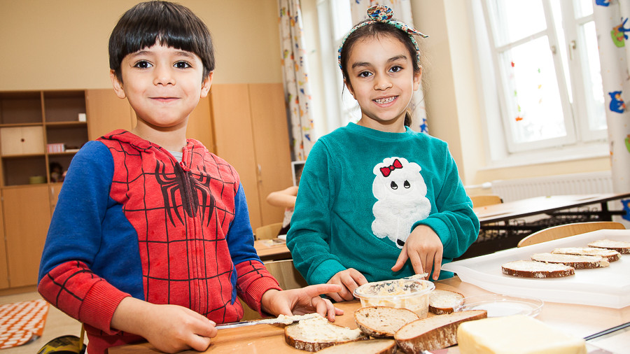 Zwei Kinder bereiten gemeinsam ein Brot mit Aufstrich zu.