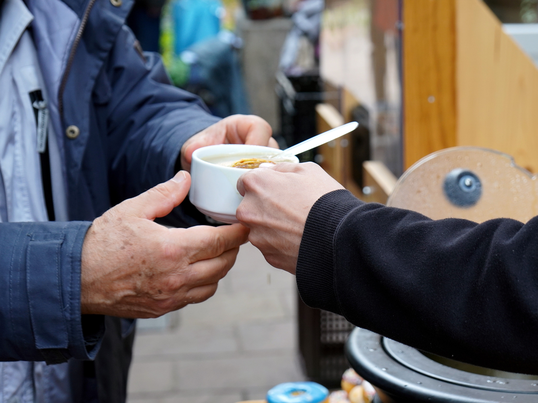 Ein Mitarbeiter im 's Häferl der Diakonie überreicht einem Gast draußen eine warme Suppe