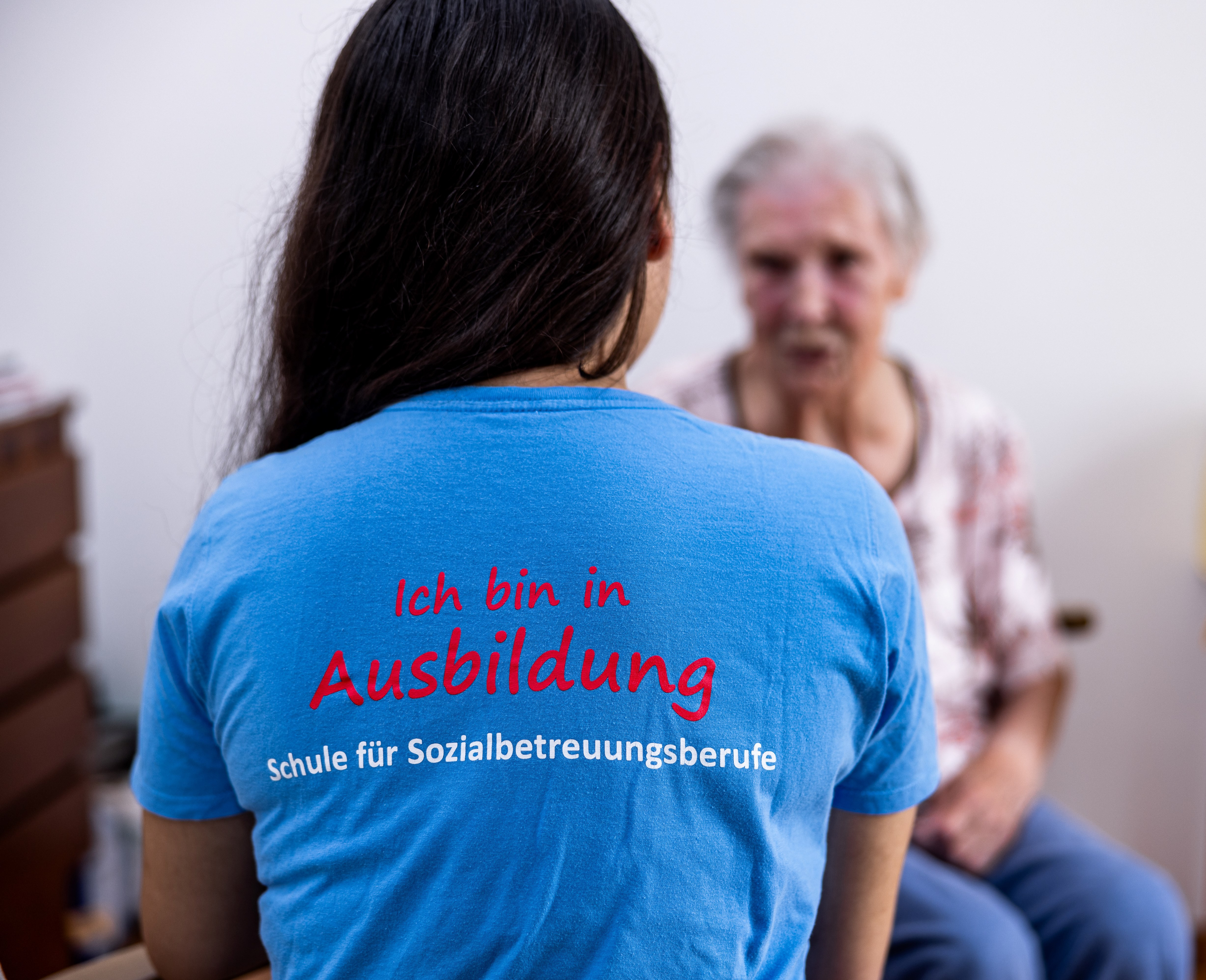 Person mit T-Shirt mit Aufschrift "Ich bin in Ausbildung" sitzt mit dem Rücken zur Kamera.