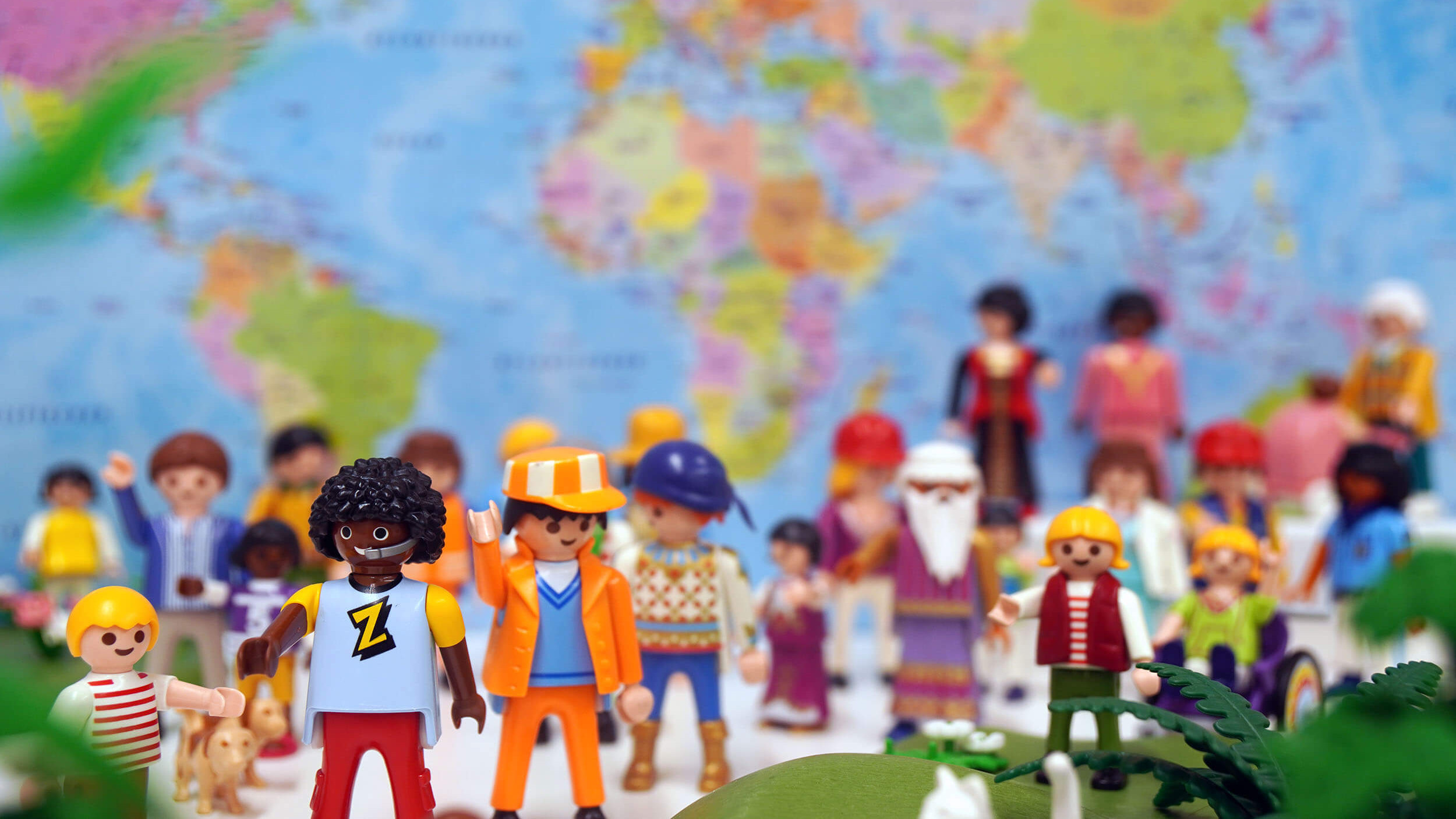 Viele bunte Spielfiguren vor einer bunten Landkarte.