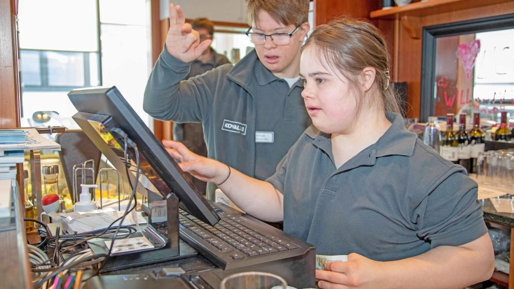 Junge Frau arbeitet mit Kollege an der Kasse in einem Cafe