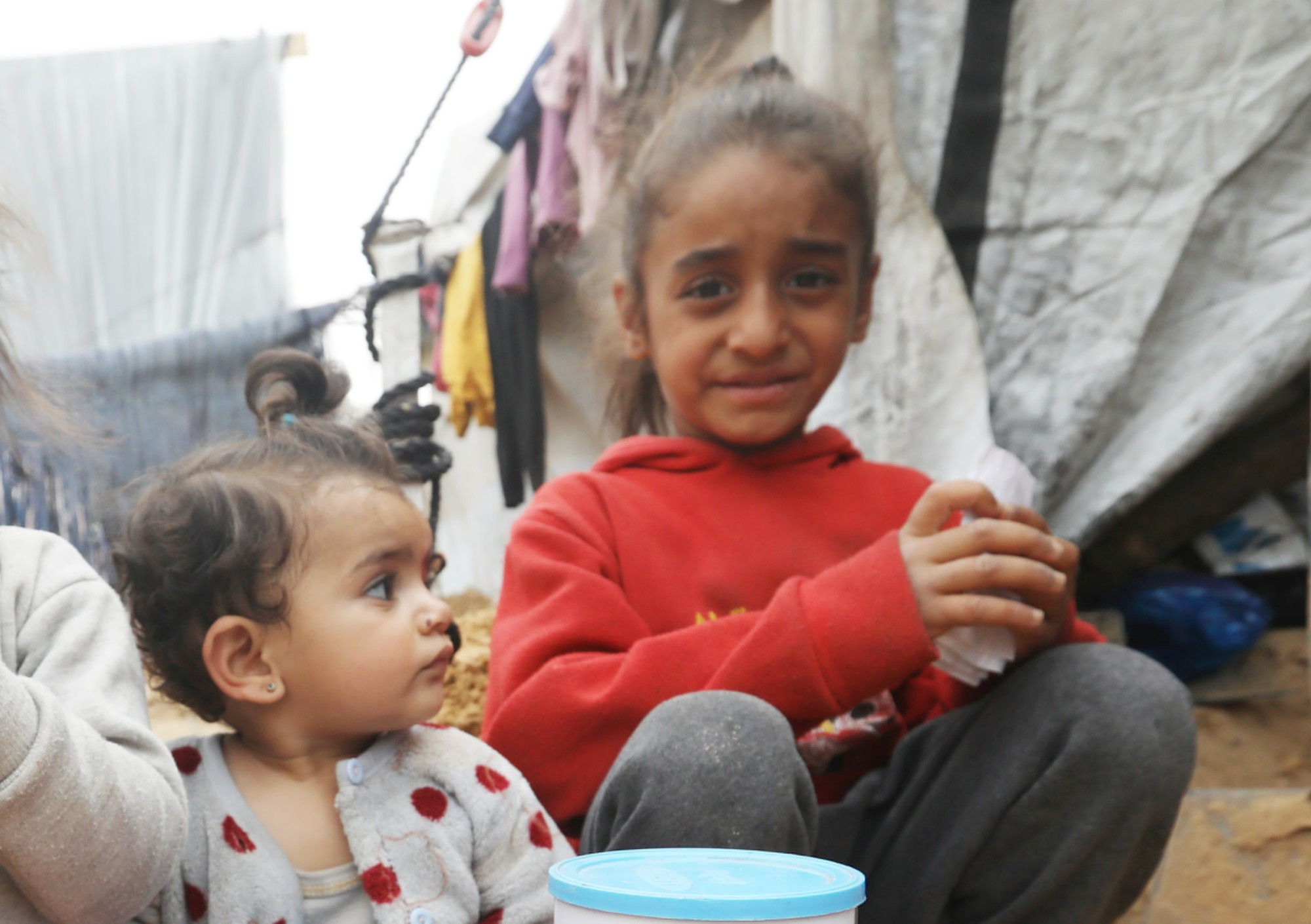 Kinder sitzen in Zeltlager auf dem Sandboden.