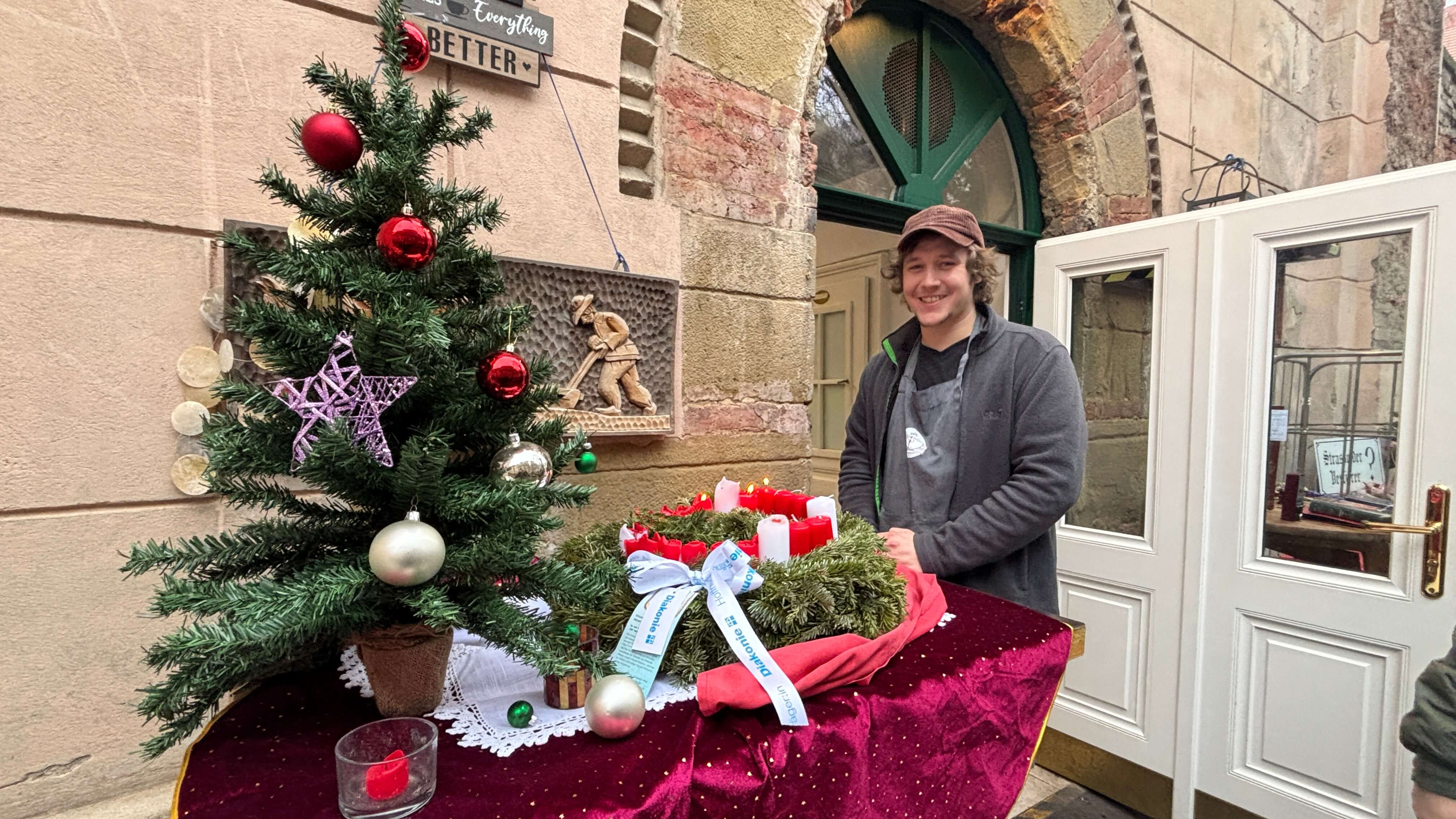 Häferl-Wirt Tobias Riener mit einem Diakonie-Adventkranz vor den öffenen Türen des Häferl.