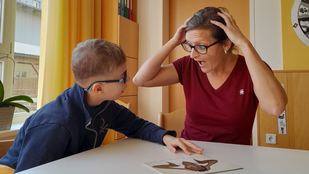 Hortbetreuerin sitzt mit einem Kind am Tisch und spricht über Gefühle.