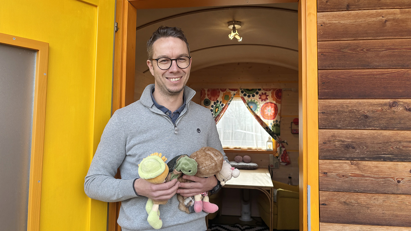 Ein Mann lächelt in die Kamera und hält Handpuppen in den Händen.