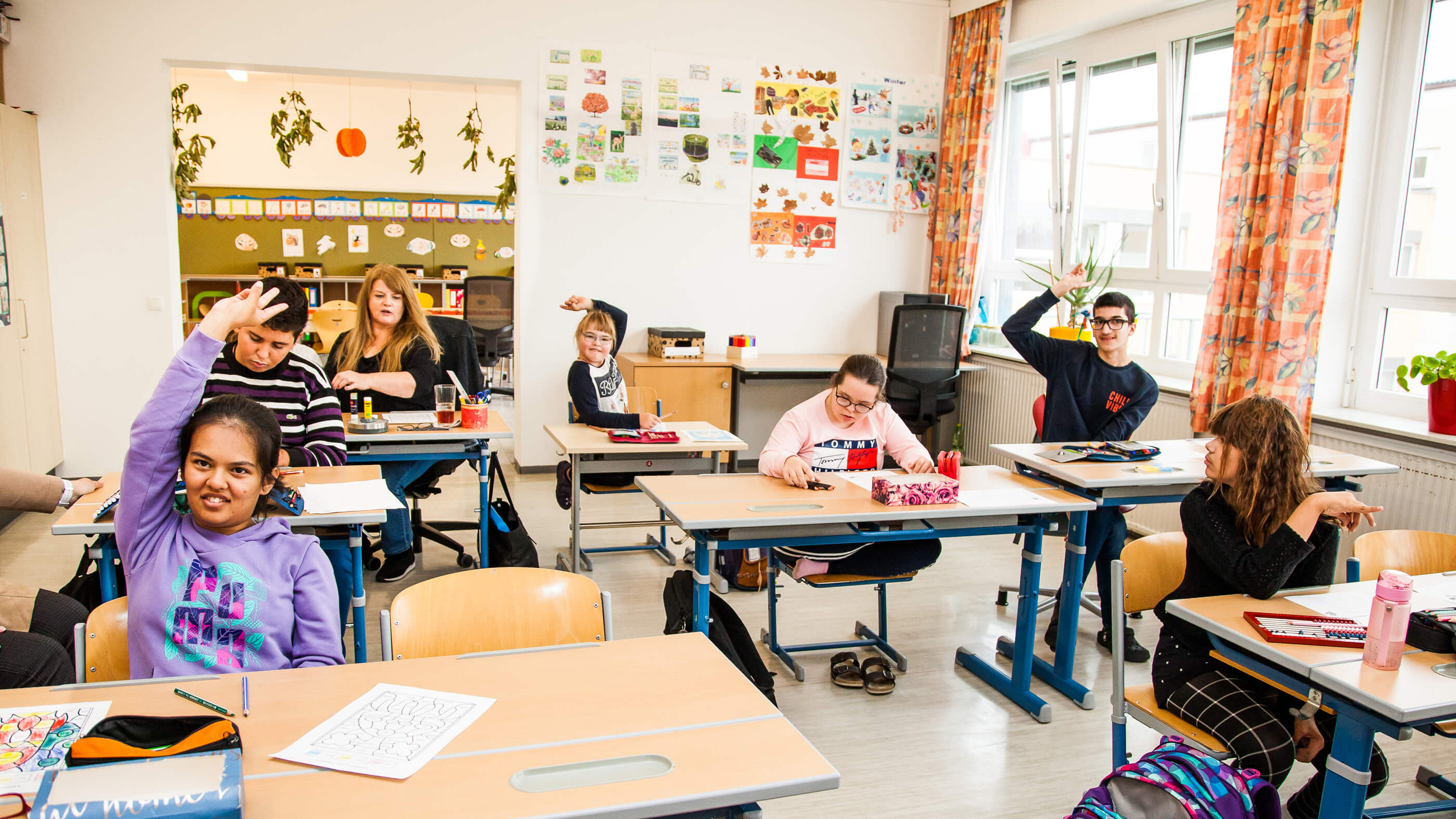 Eine Schulkasse mit Schüler:innen. EInige der Schüler:innen zeigen auf. Eine der Schüler:innen ist Hoffnungsträgerin Lili.