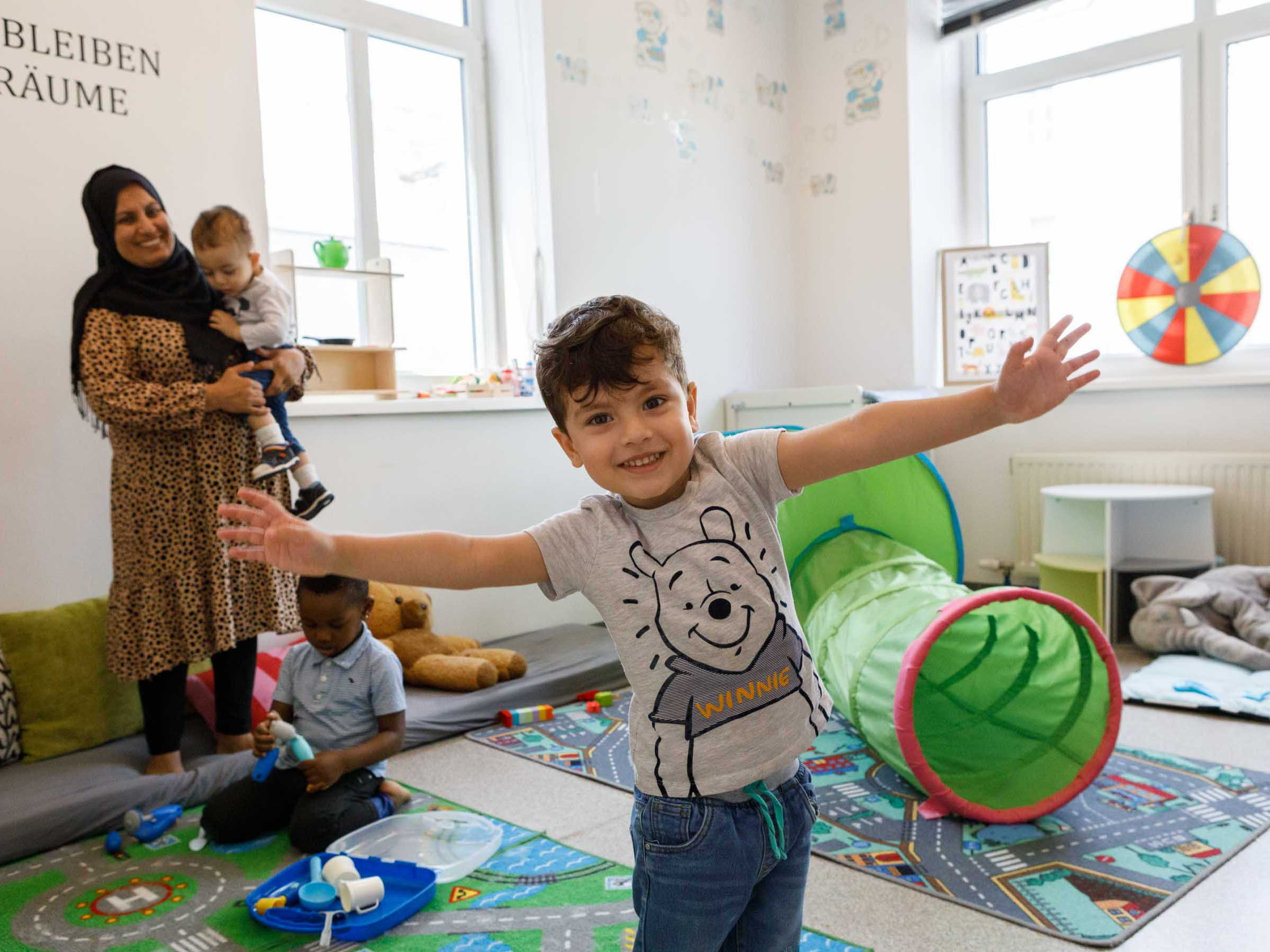 Ein lachendes Kind steht mit ausgestreckten Armen im Spielzimmer von MaBa