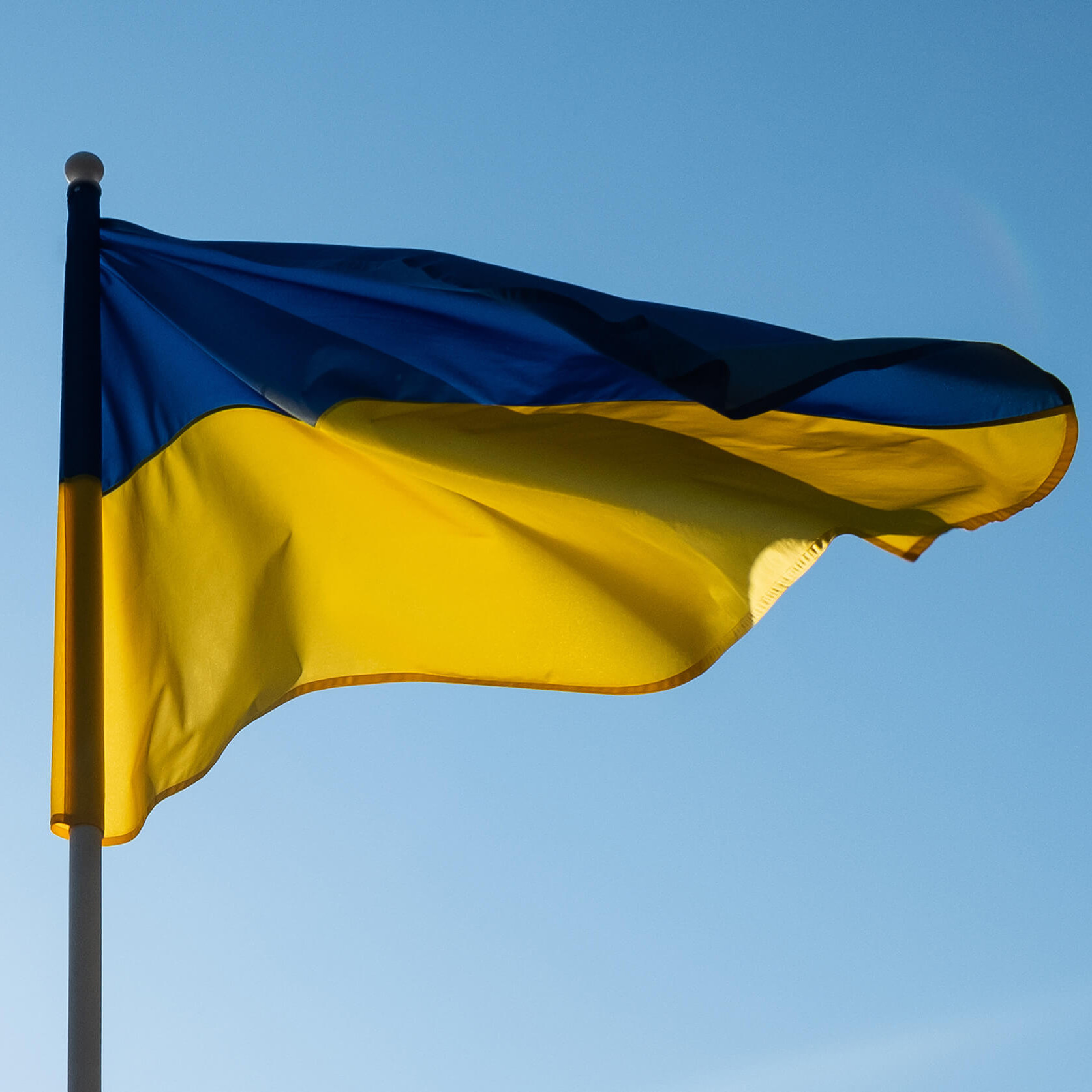 Eine Ukraine-Fahne im Wind vor blauem Himmel.