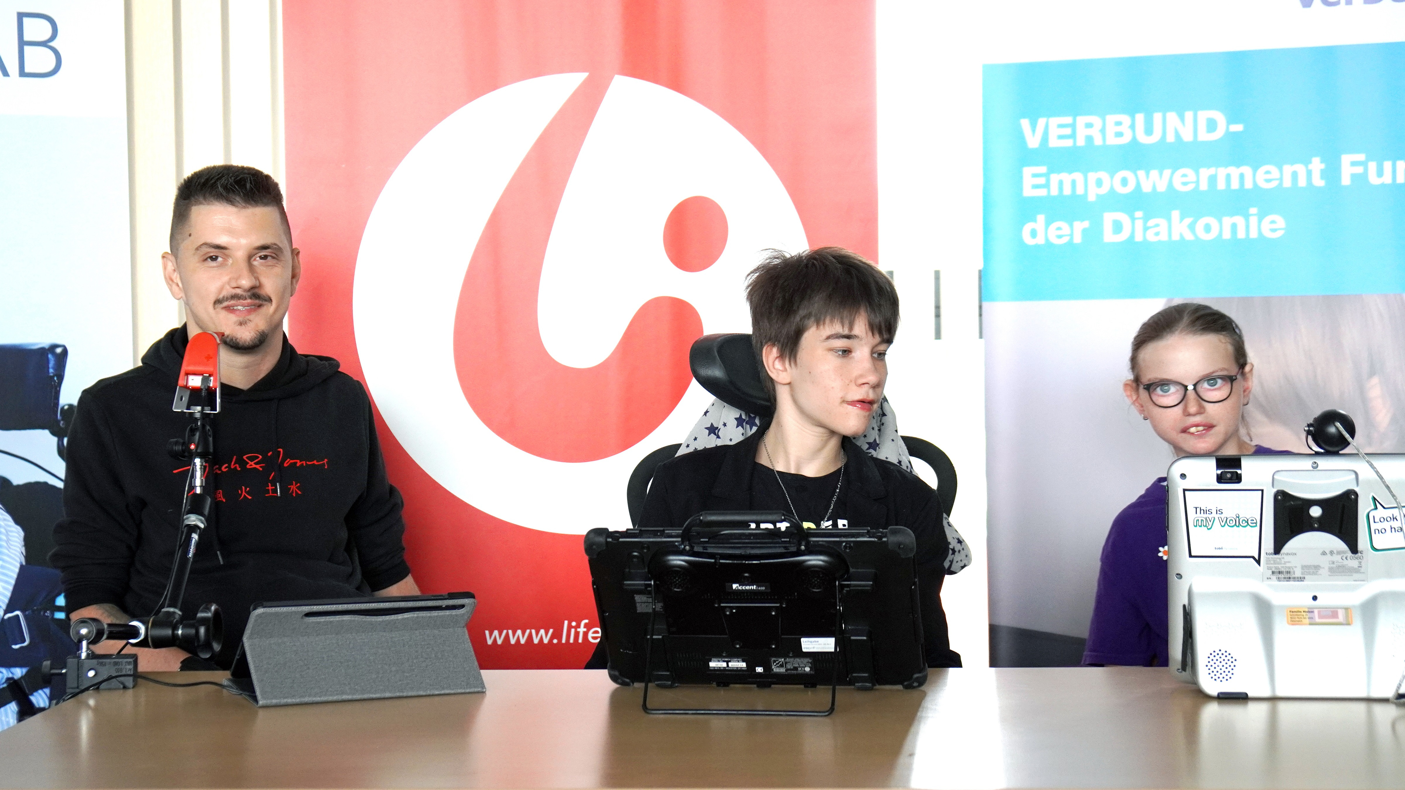 Ein Mann und zwei junge Frauen im Rollstuhl bei einem Pressetermin