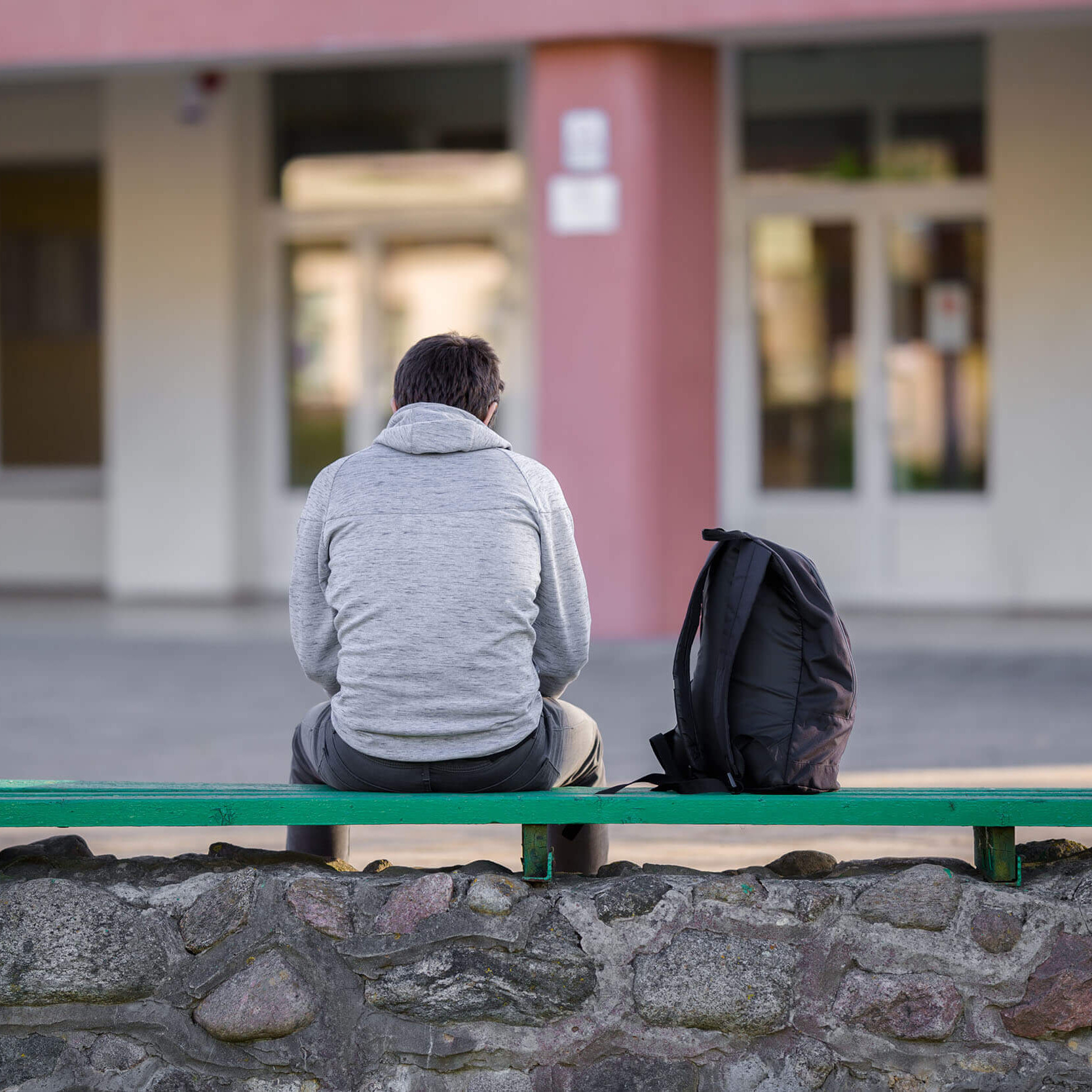 Ein Jugendlicher auf einer Parkbank vor einer Schule