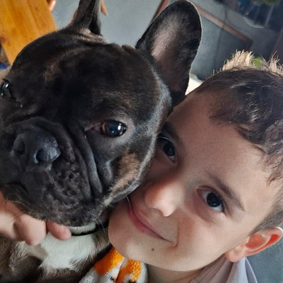 Ein Junge lächelt in die Kamera, daneben ein braun gefleckter Hund, der ebenfalls in die gleiche Richtung blickt.