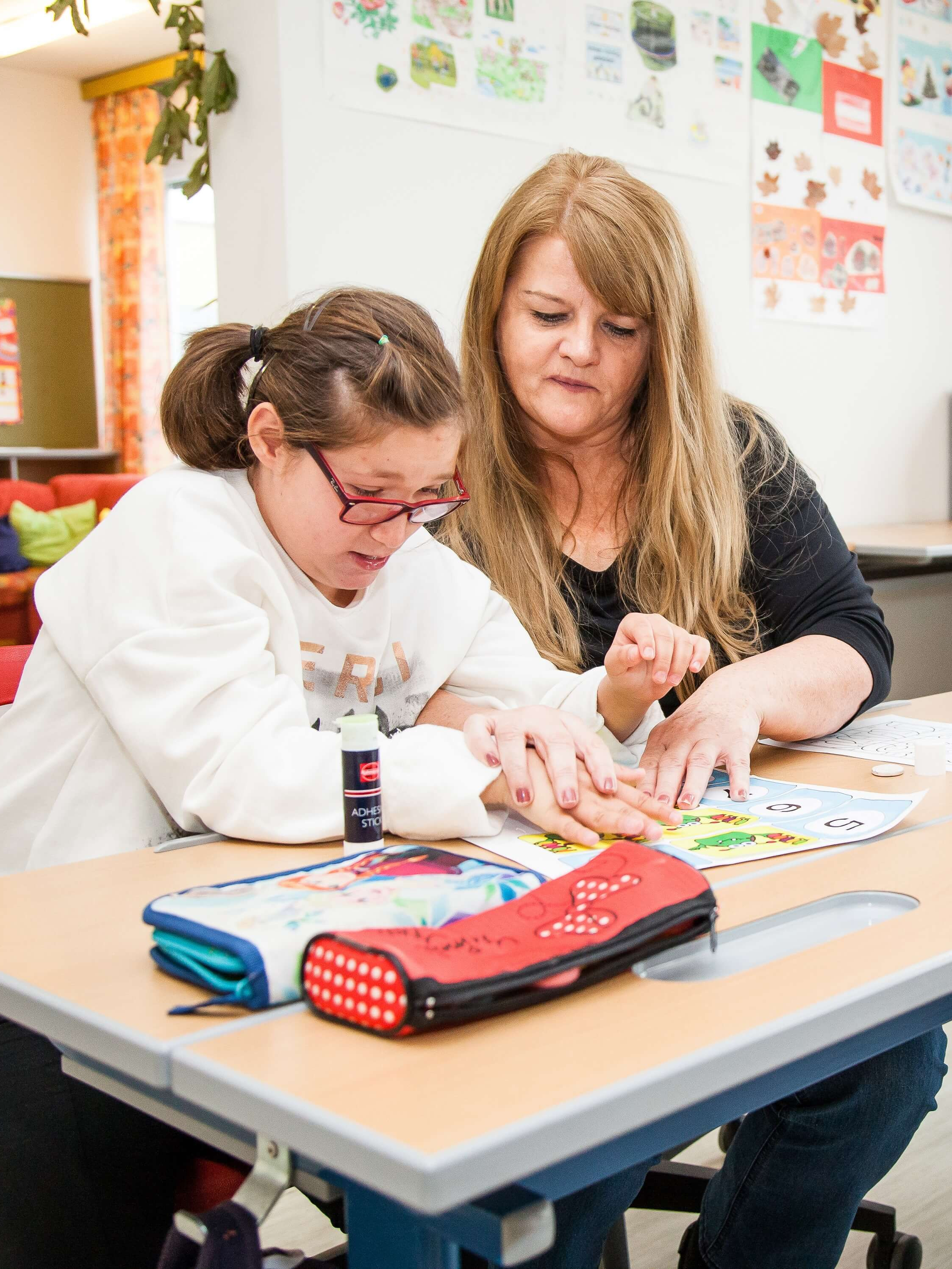 Eine Schulassistentin der Diakonie unterstützt ein Mädchen beim Lernen in der Schule.