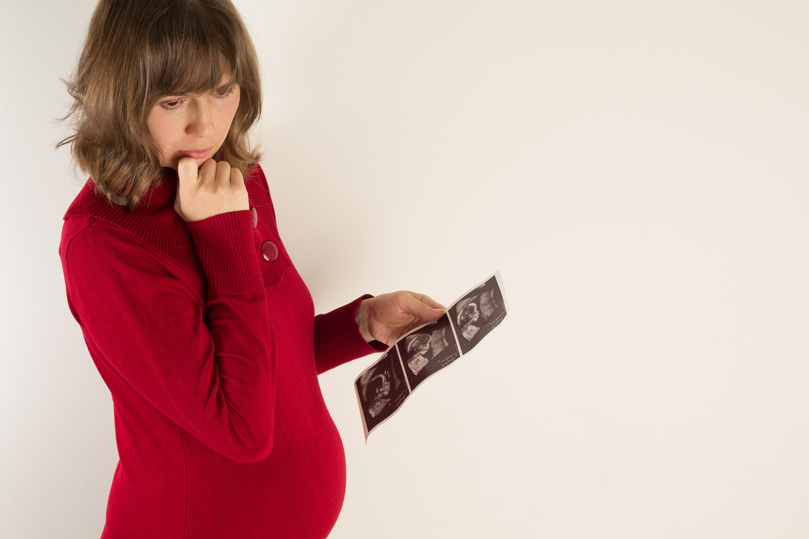 Schwangere Frau mit sorgenvollem Blick und Ultraschallbildern ihres Babys.