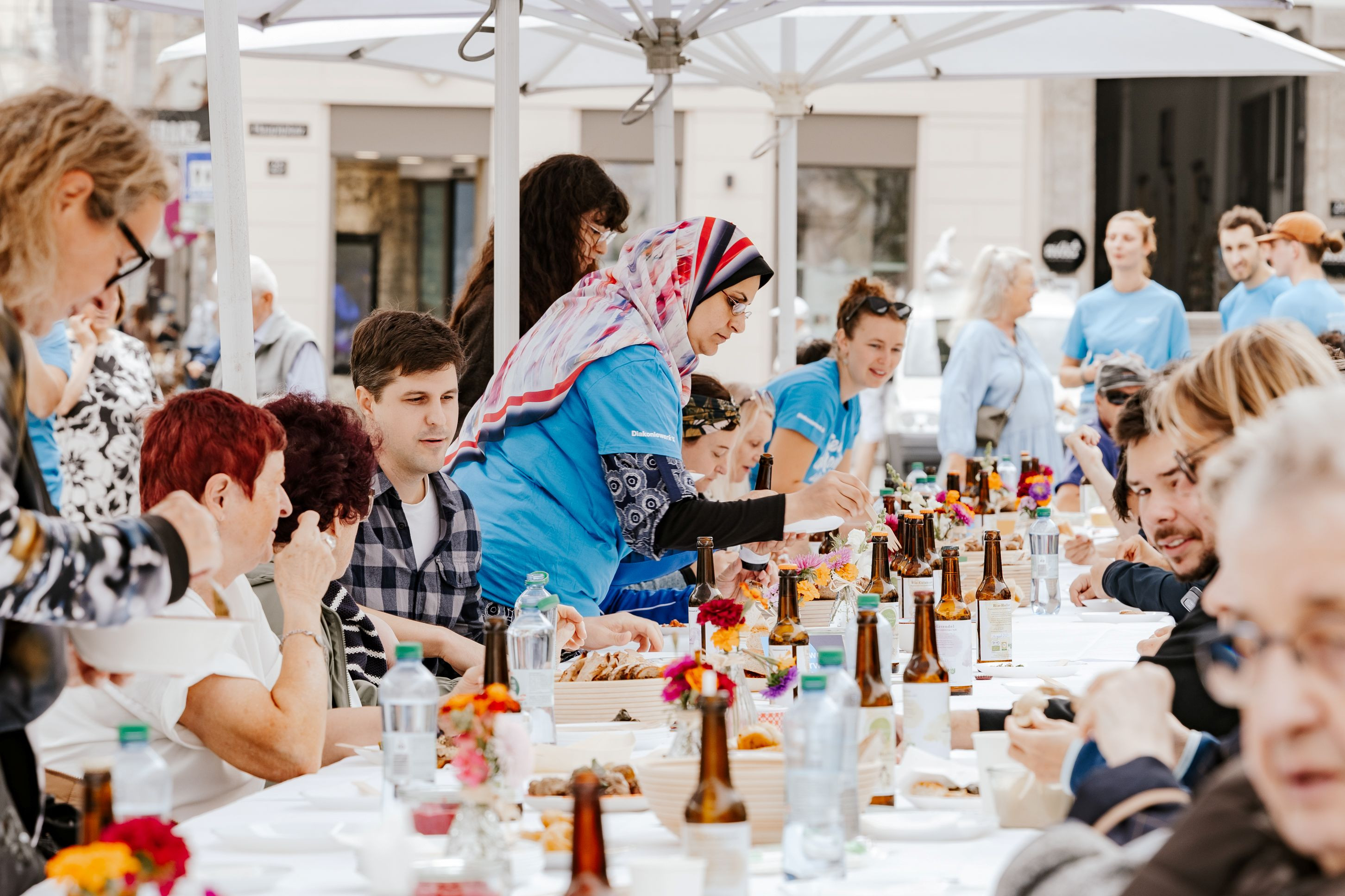 Viele Menschen an einer langen Tafel mit Getränken und Speisen beim Tisch der Vielfalt des Diakoniewerks in Linz.