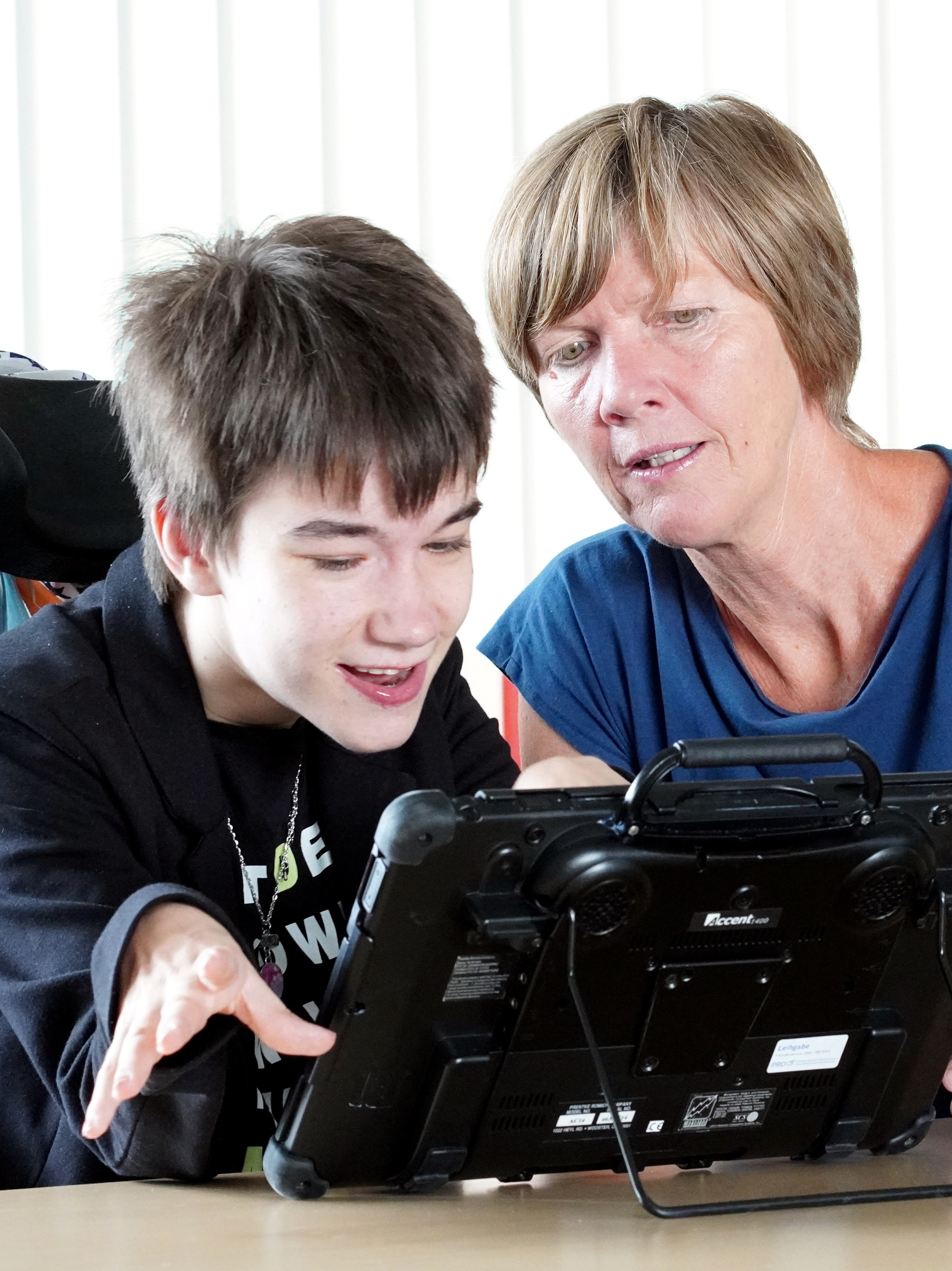 Eine junge Frau mit Sprachcomputer und eine Mitarbeiterin der Diakonie unterhalten sich.