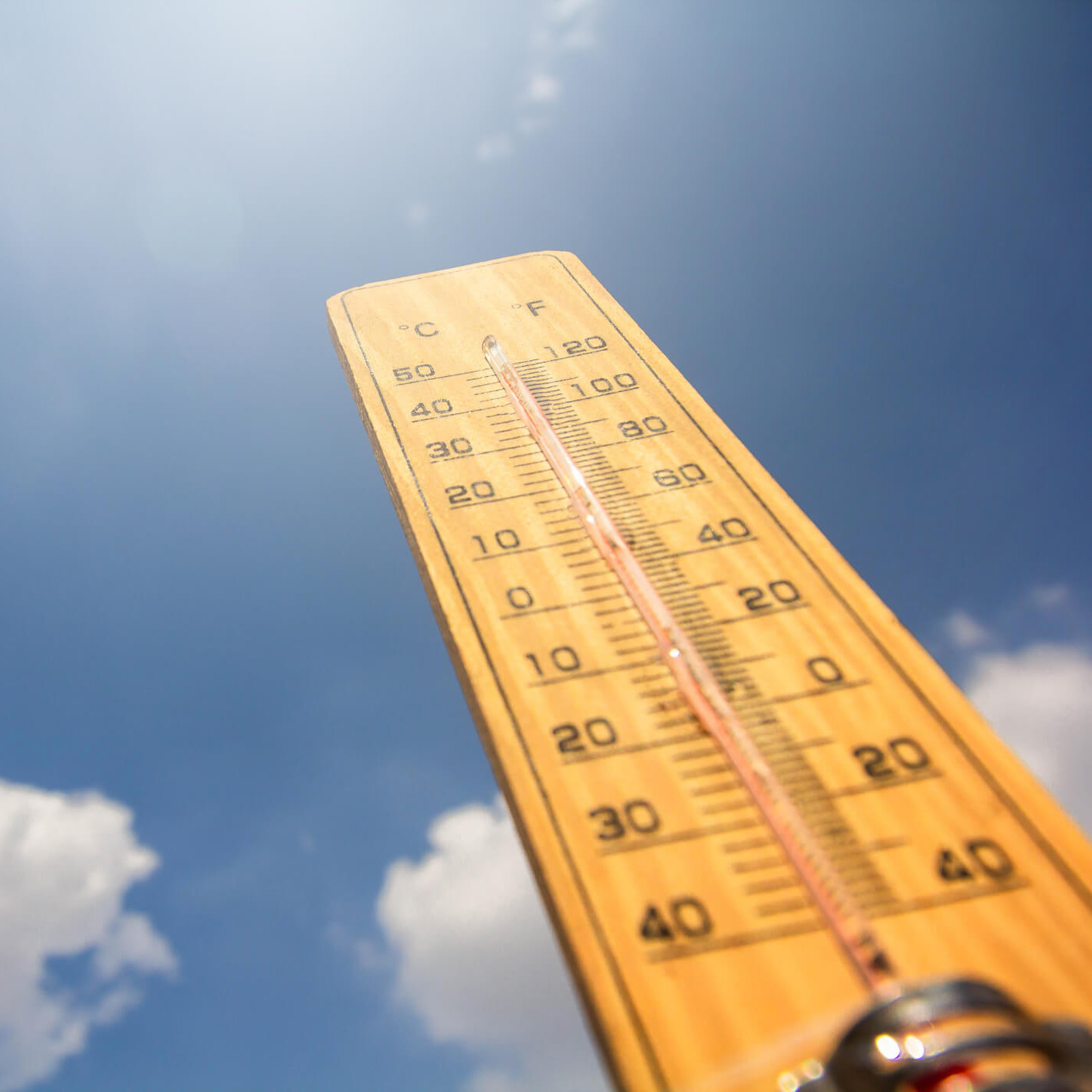 Die Sonne scheint, der Himmel ist blau und ein paar weiße Wolken ziehen vorbei. Daneben steht ein Thermometer, das in den Himmel zeigt.